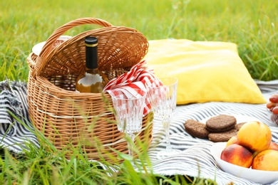 Photo of Wicker picnic basket with wine and glasses on blanket outdoors