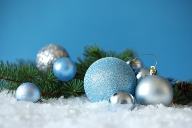 Photo of Beautiful Christmas balls and fir branch on snow against blue background. Space for text