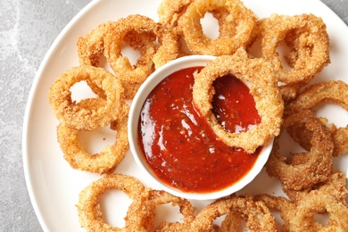 Photo of Homemade crunchy fried onion rings with sauce on color table, top view