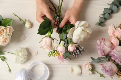 Photo of Florist creating beautiful bouquet at white table, top view
