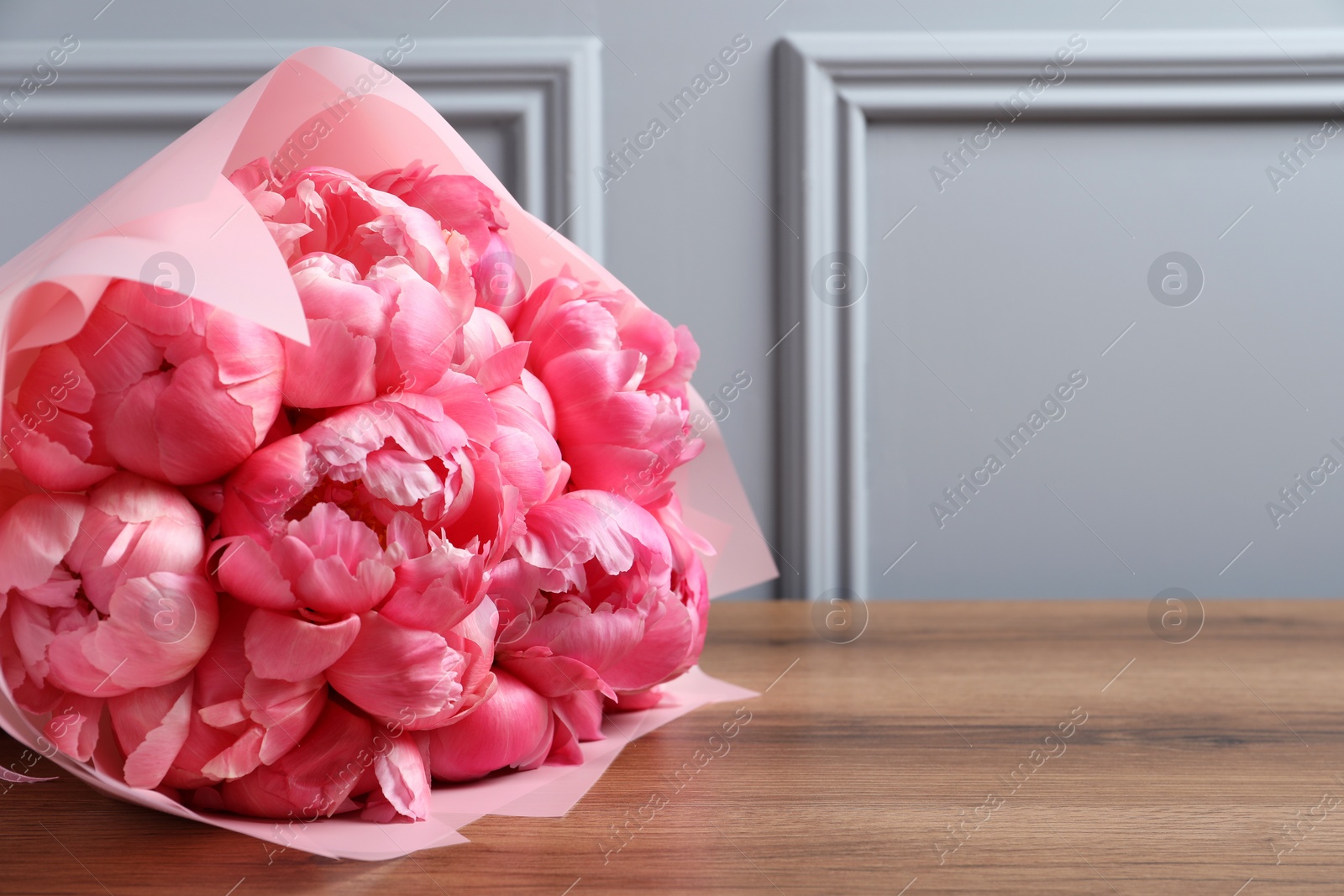 Photo of Bouquet of beautiful pink peonies on wooden table near grey wall. Space for text