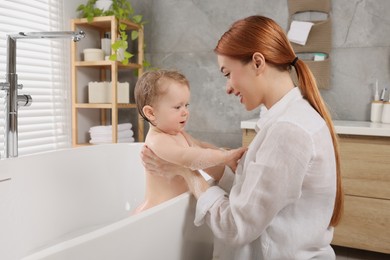 Mother washing her little baby in tub at home