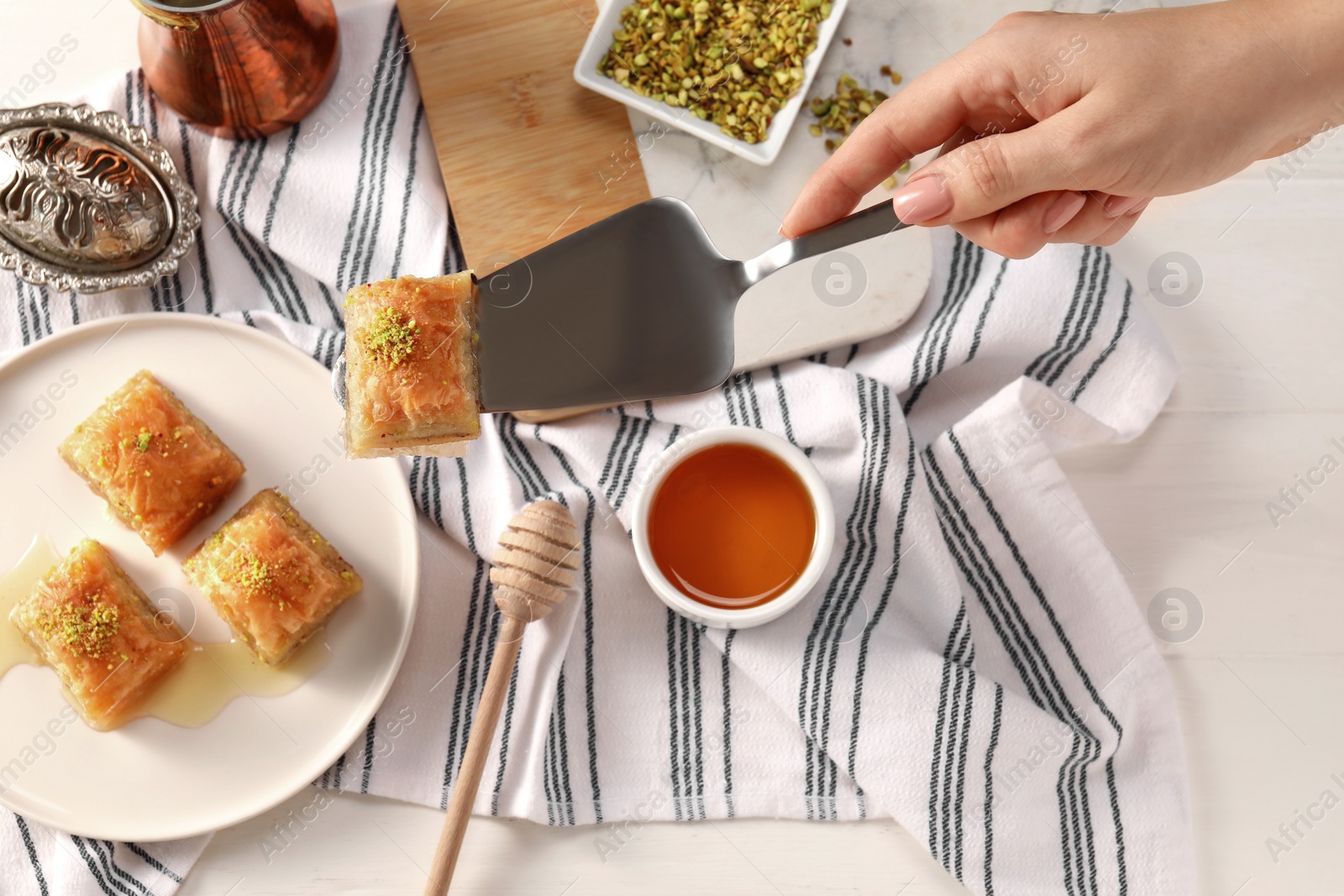 Photo of Woman serving delicious sweet baklava at white table, top view