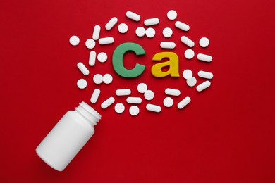 Photo of Pills, open bottle and calcium symbol made of colorful letters on red background, flat lay