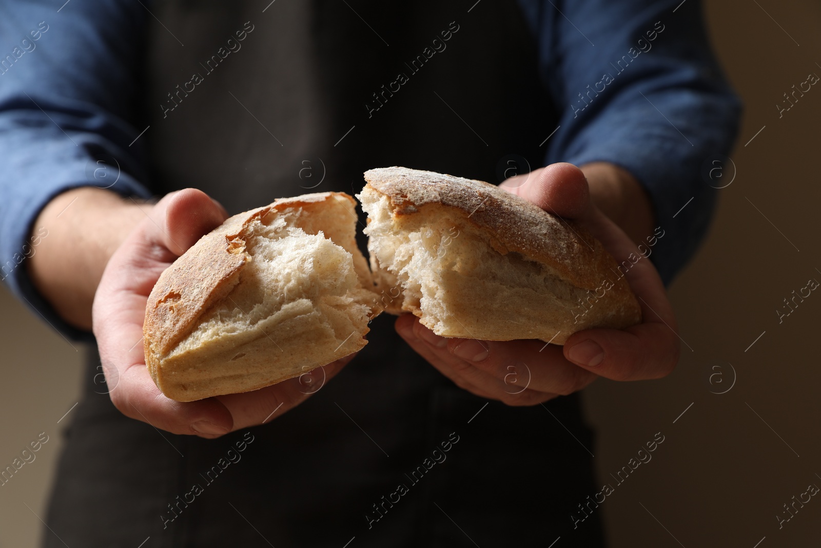 Photo of Man breaking loaf of fresh bread on dark background, closeup