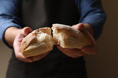 Man breaking loaf of fresh bread on dark background, closeup