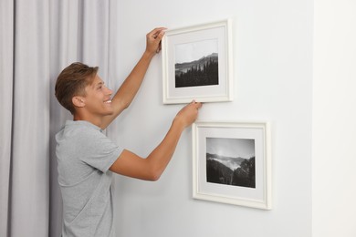 Young man hanging picture frames on white wall indoors