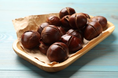 Photo of Fresh edible sweet chestnuts in serving plate on light blue wooden table
