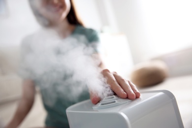 Woman using modern air humidifier at home, closeup