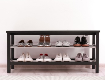 Photo of Shoe rack with different footwear near white wall. Stylish hallway interior