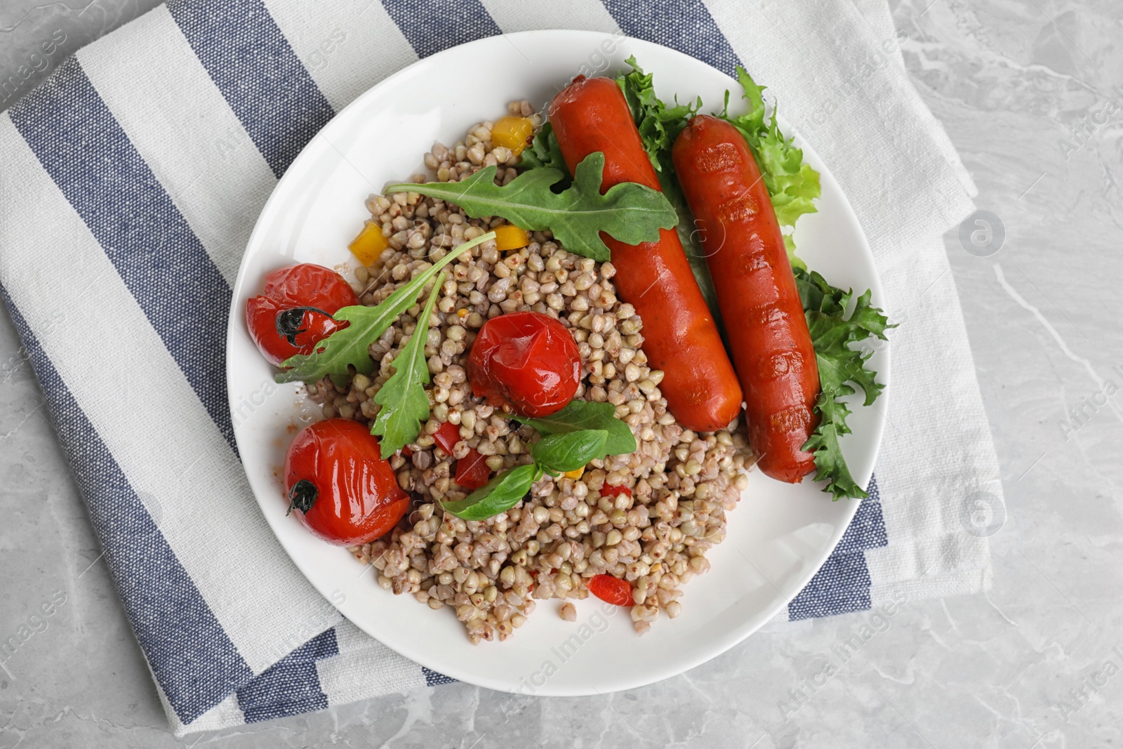 Photo of Tasty buckwheat porridge with sausages on light grey marble table, top view