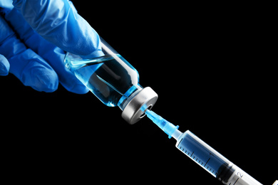 Photo of Doctor filling syringe with medication on black background, closeup. Vaccination and immunization