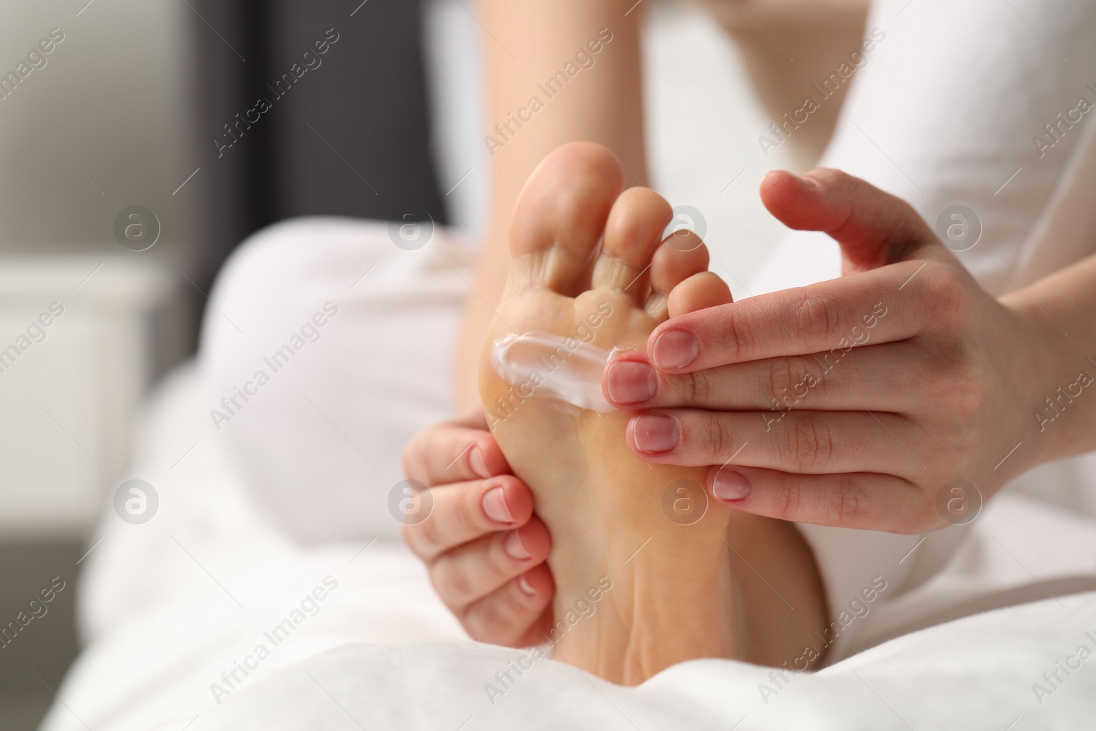Photo of Young woman with dry skin applying cream onto her foot indoors, closeup