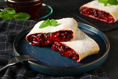 Photo of Delicious strudel with cherries, powdered sugar and mint on table, closeup