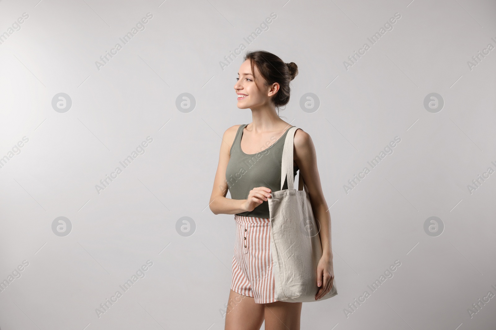 Photo of Happy young woman with blank eco friendly bag on light background