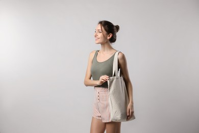 Happy young woman with blank eco friendly bag on light background