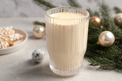 Glass of delicious eggnog and fir branch on light table, closeup