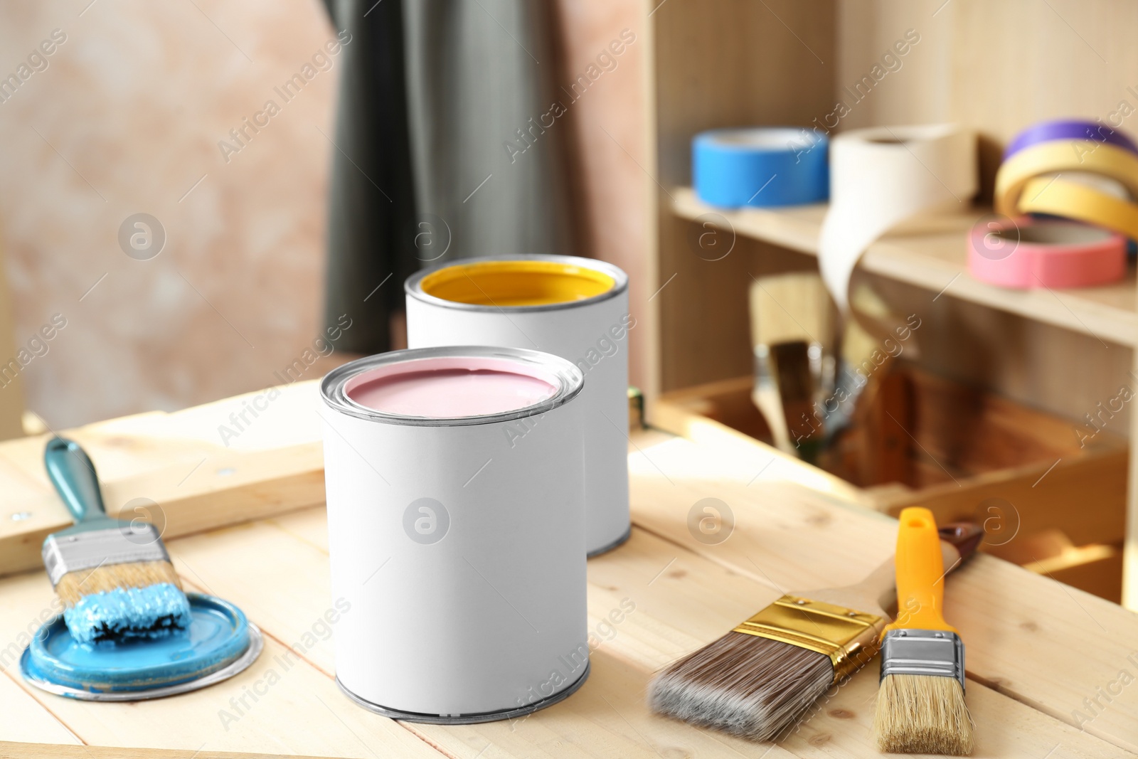 Photo of Cans of colorful paints and brushes on wooden table indoors