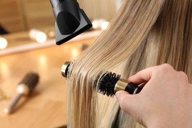 Hairdresser blow drying client's hair in salon, closeup