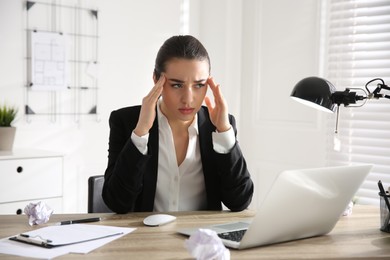 Photo of Stressed and tired young woman with headache at workplace