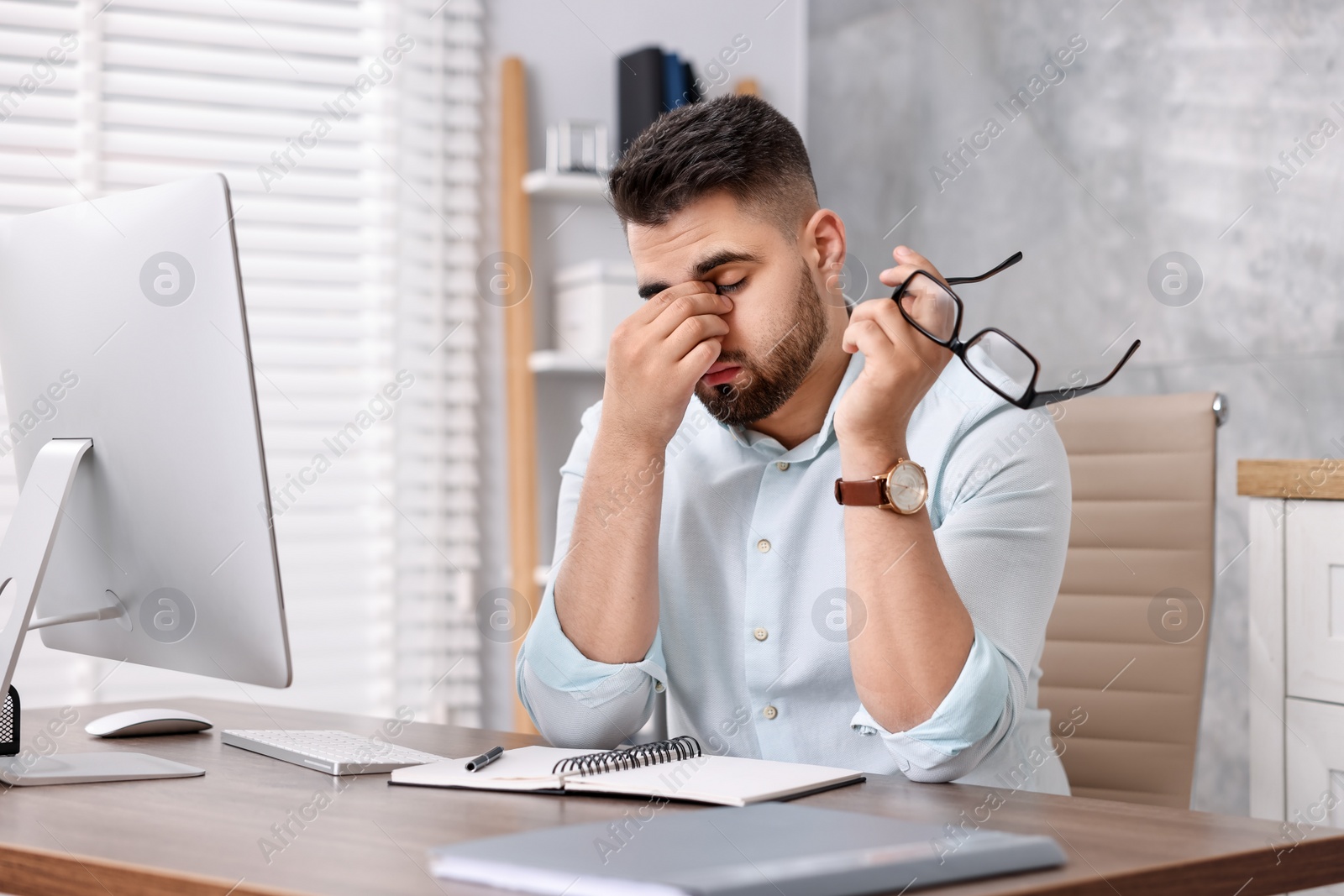 Photo of Overwhelmed man with glasses sitting at table in office