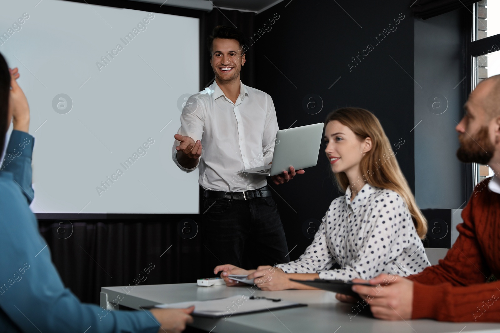 Photo of Business people listening to speaker in conference room with video projection screen