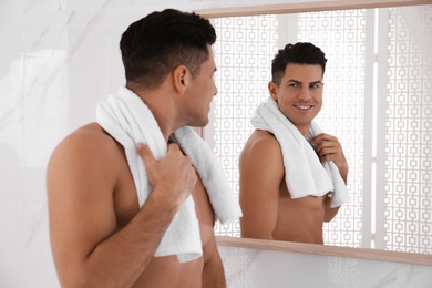 Photo of Handsome man with towel near mirror in bathroom