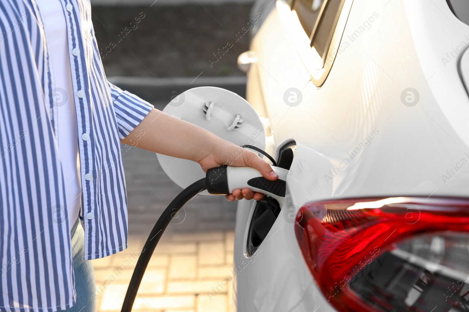 Photo of Woman inserting plug into electric car socket at charging station, closeup