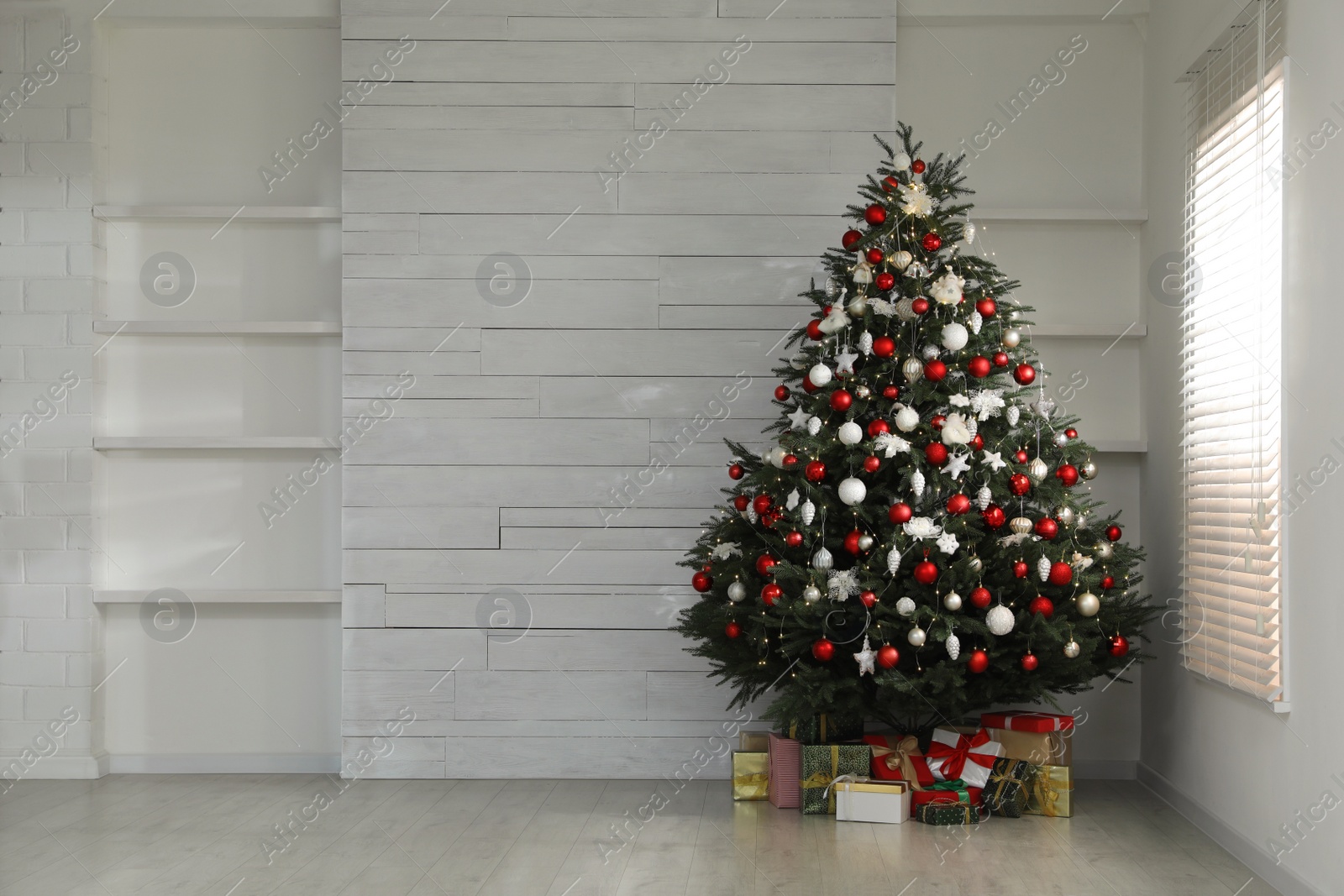 Photo of Beautifully decorated Christmas tree and gifts near window in empty room, space for text