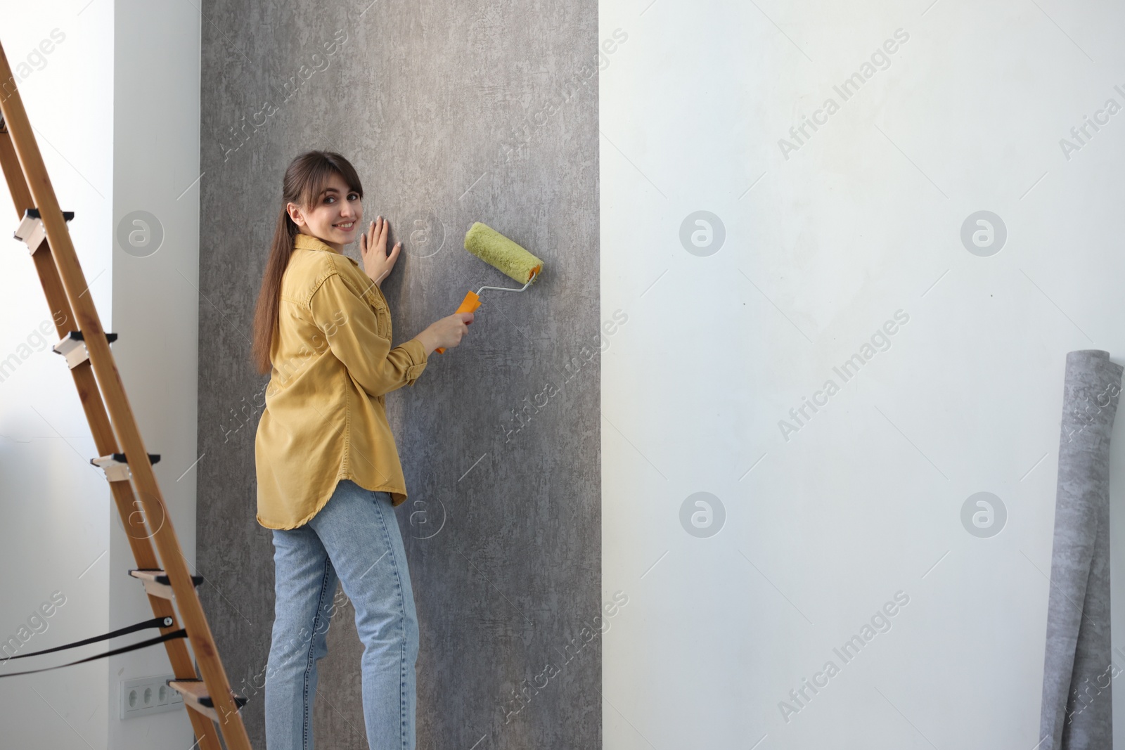 Photo of Woman hanging stylish gray wallpaper in room