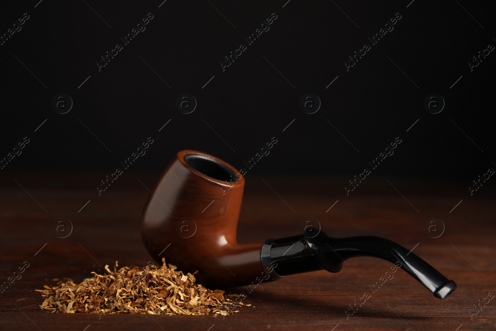 Photo of Pile of tobacco and smoking pipe on wooden table against dark background. Space for text