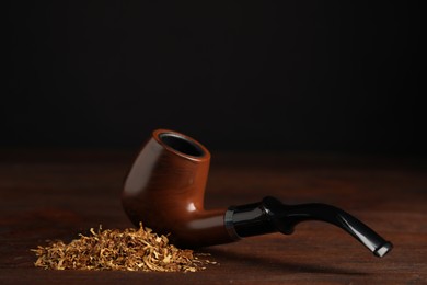 Pile of tobacco and smoking pipe on wooden table against dark background. Space for text