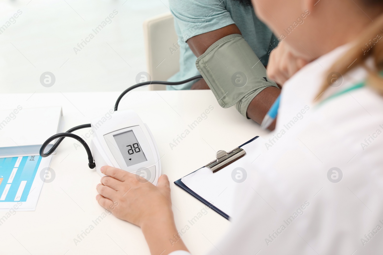 Photo of Young doctor checking African-American patient's blood pressure in hospital