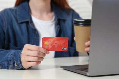 Woman with credit card using laptop at white table, closeup