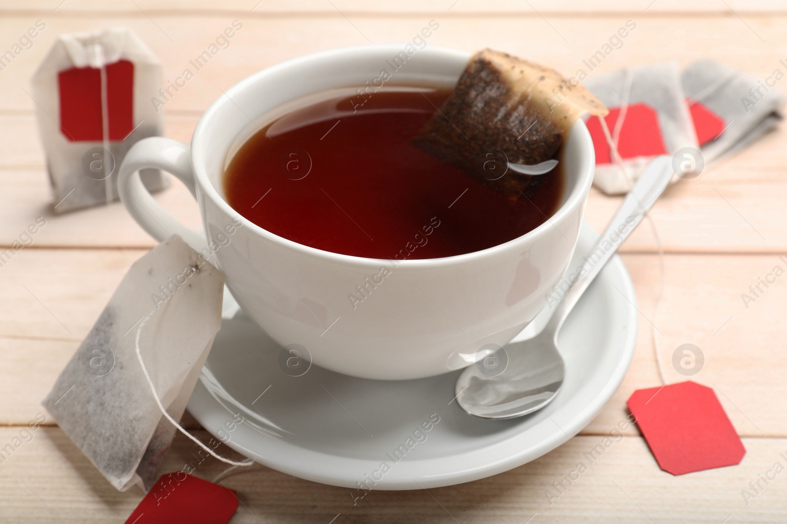 Photo of Tea bags, cup of hot beverage and spoon on light wooden table, closeup