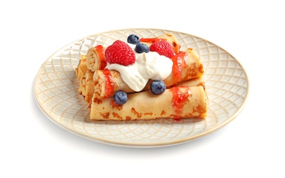 Thin pancakes with syrup, cream and berries on plate against white background