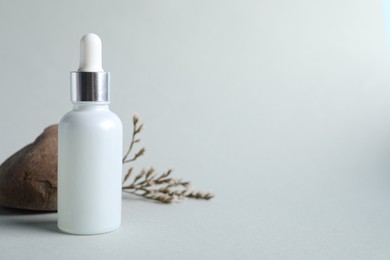 Photo of Bottle with cosmetic serum, stone and dry flowers on light grey background, space for text