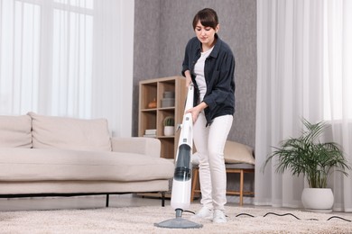 Young housewife vacuuming carpet at home. Cleaning chores