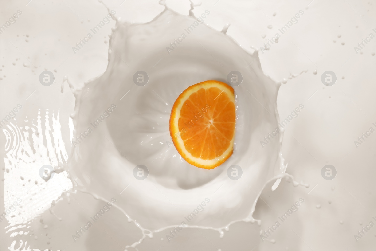 Photo of Slice of orange falling in milk with splash, top view