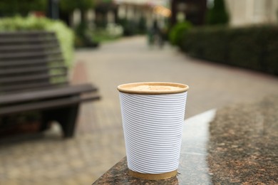 Photo of Paper cup of coffee near fountain outdoors. Takeaway drink
