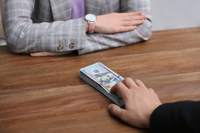 Photo of Man offering bribe money to woman at table, closeup