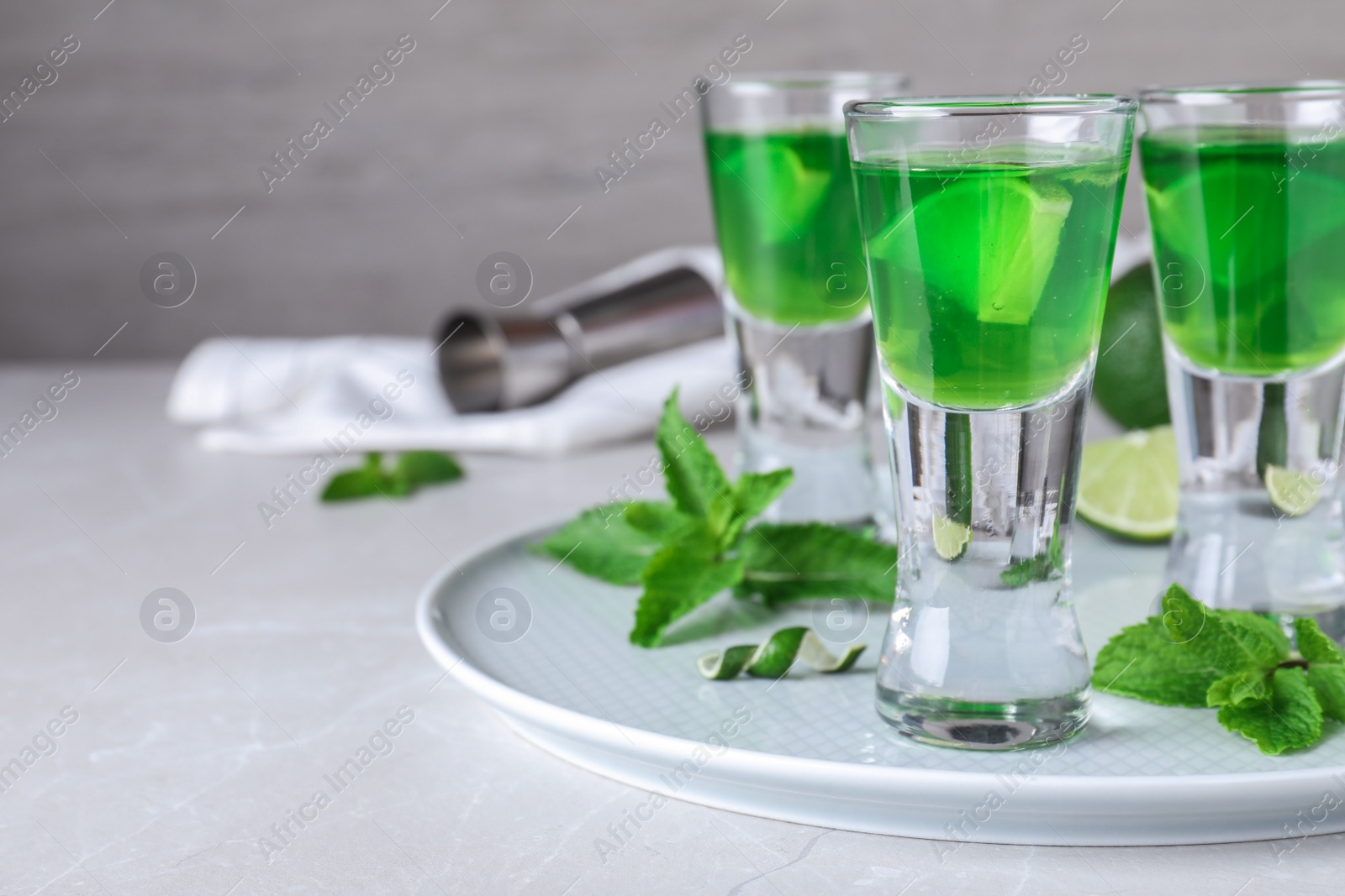 Photo of Delicious mint liqueur with lime and green leaves on white table. Space for text