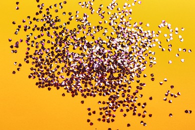 Photo of Shiny bright violet glitter on yellow background, flat lay
