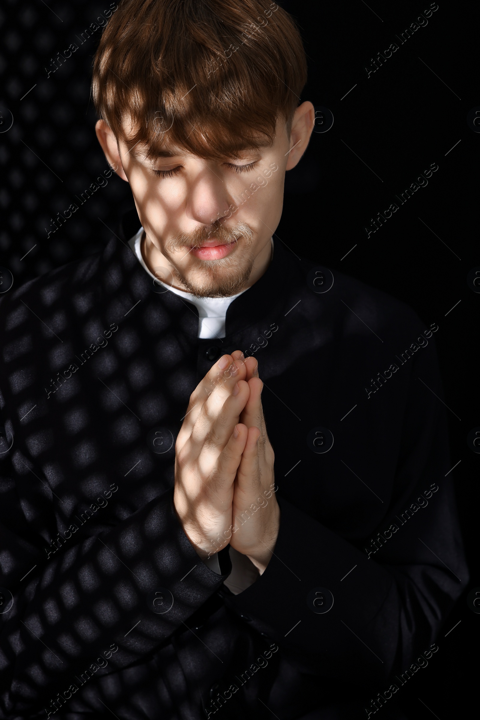 Photo of Catholic priest in cassock praying in confessional