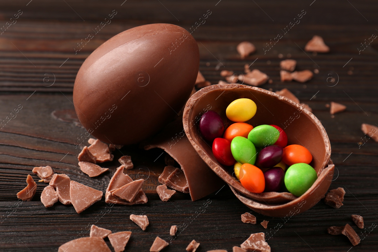 Photo of Broken and whole chocolate eggs with sweets on wooden table