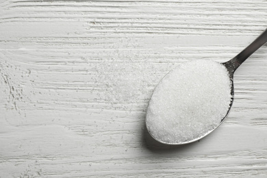 Spoon of sugar on white wooden table, top view. Space for text