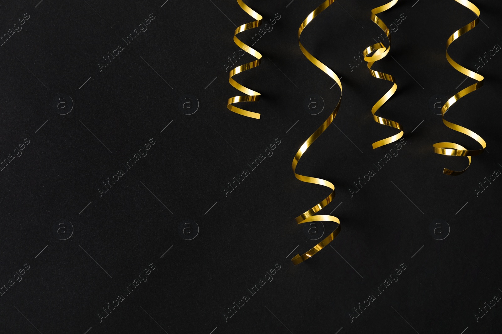 Photo of Shiny golden serpentine streamers on black background, flat lay. Space for text