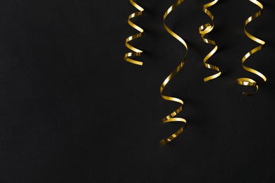 Shiny golden serpentine streamers on black background, flat lay. Space for text