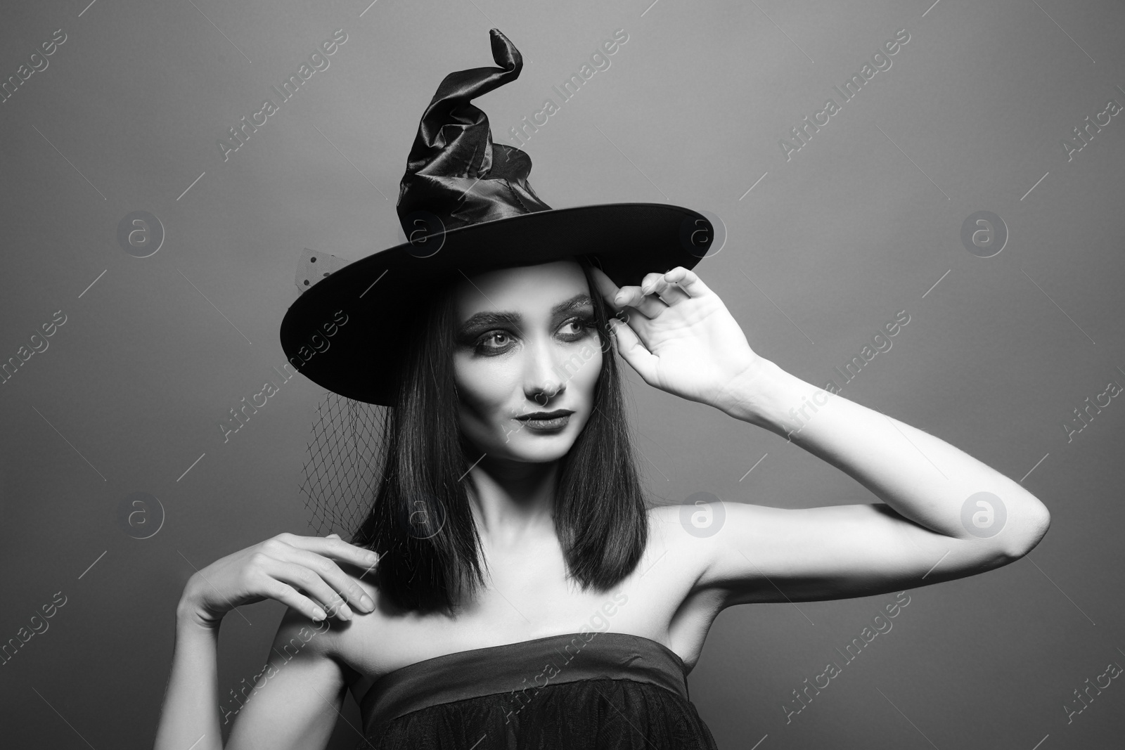 Photo of Mysterious witch wearing hat on dark background. Black and white effect