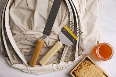 Photo of Different beekeeping tools and jar of honey on white table, flat lay